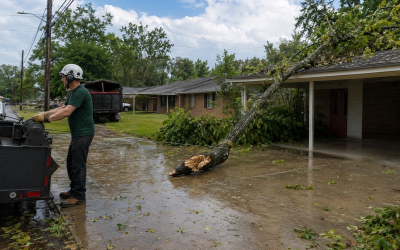 Worker at the winch drum drawing a storm-broken chinkapin oak leader off a Smyrna carport roof.